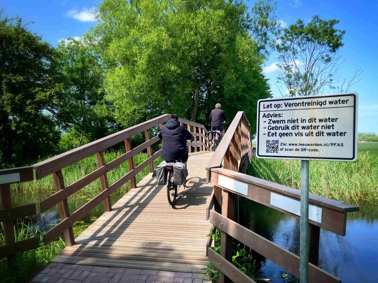 PFAS-vervuiling Jelsumer Feart Leeuwarden Foto Wetterskip Fryslân-klein brug over Jelsumer Feart met bord en 2 fietsers op de brug